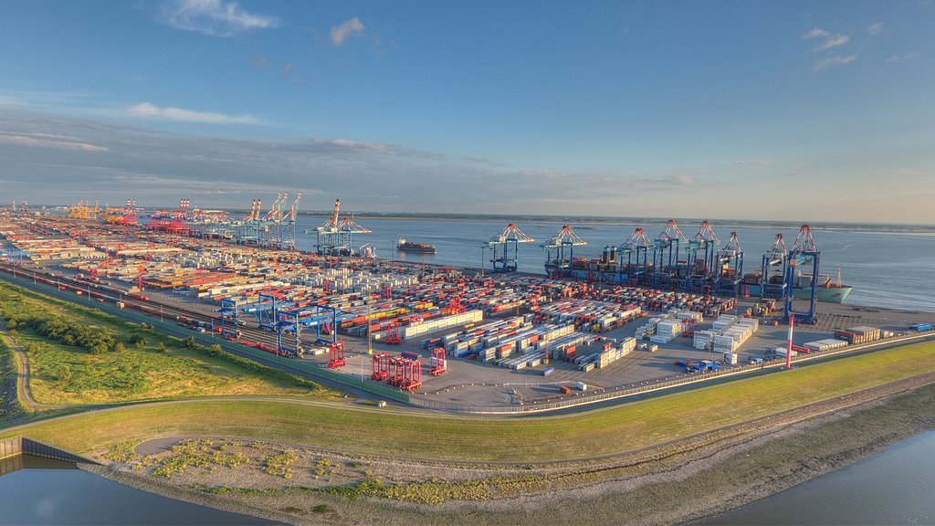 Weitläufiger Containerhafen mit Krananlagen und Schiffen am Ufer eines ruhigen Meeres.