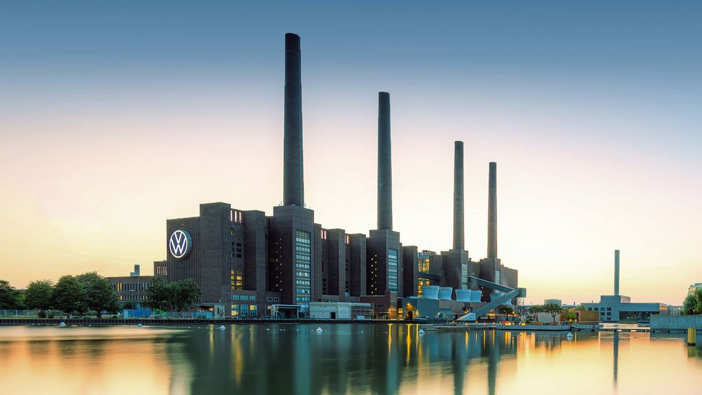 Volkswagen-Industriegebäude mit vier Schornsteinen bei Sonnenuntergang, Spiegelung im Wasser.